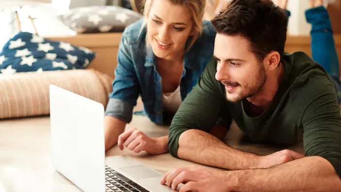 Pareja joven usando un ordenador portátil en casa para realizar gestiones online en un ambiente relajado.