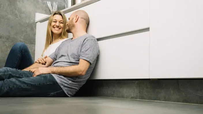 Pareja sonriente en el suelo de su nueva cocina, cumpliendo el sueño de su primera vivienda.