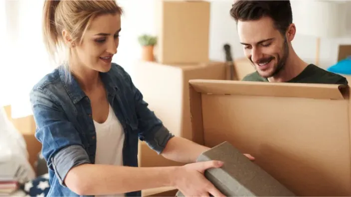 Pareja sonriente desempaquetando cajas de cartón en su nuevo hogar durante una mudanza familiar.