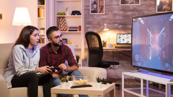 Una pareja sentada en el salón jugando a un videojuego en una televisión grande.