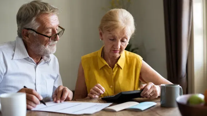 Pareja de jubilados calculando gastos o pensión con facturas y calculadora en casa.