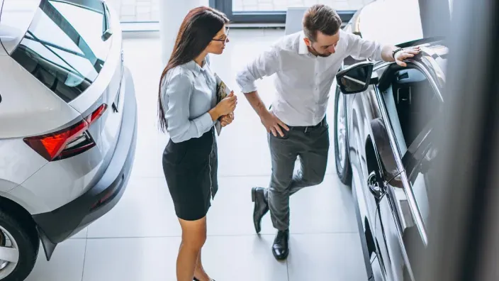 Vendedora mostrando coche nuevo a cliente interesado en concesionario de automóviles.