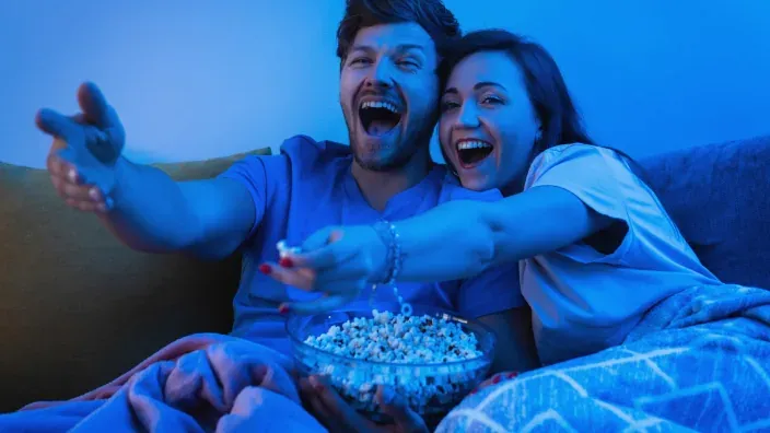 Pareja comiendo palomitas y disfrutando de una película en el sofá para ver cine y series en streaming desde casa.