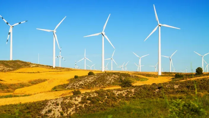 Aerogeneradores en funcionamiento en un parque eólico sobre colinas doradas en España.