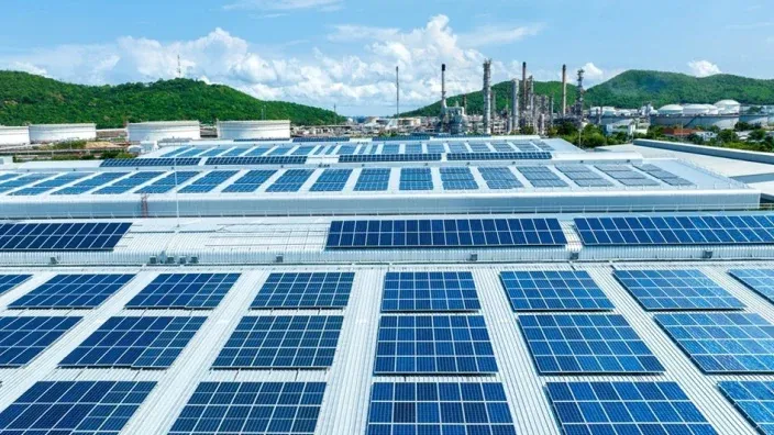 Paneles solares en primer plano con aerogeneradores al fondo en un parque híbrido de energías renovables.