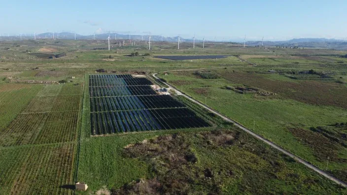 Vista aérea de un parque solar en una zona rural con aerogeneradores al fondo