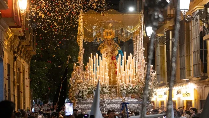 Paso de palio con una imagen religiosa y cirios durante una procesión nocturna en Málaga.