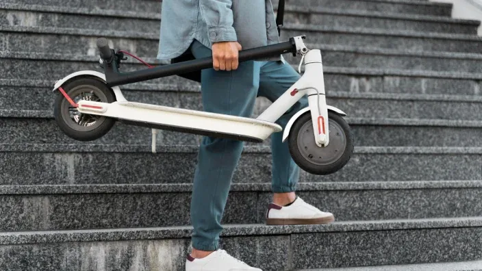 Usuario subiendo escaleras cargando un patinete eléctrico blanco plegado demostrando su ligereza.