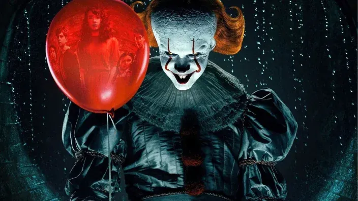 El payaso de It sosteniendo un globo rojo con reflejos de niños en su interior, en una escena de terror