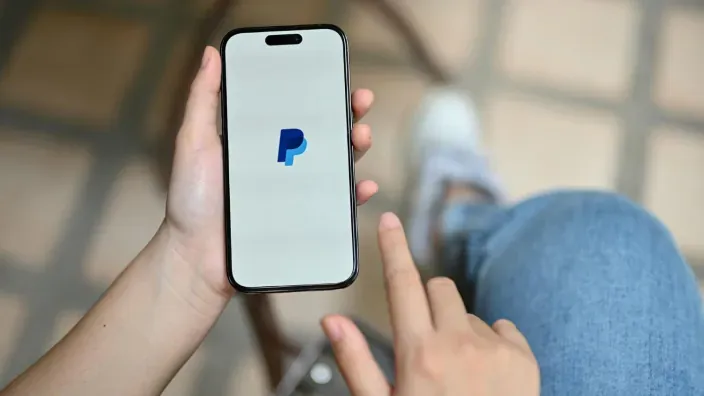 Persona usando la aplicación de PayPal en su teléfono móvil para realizar pagos y transacciones online.