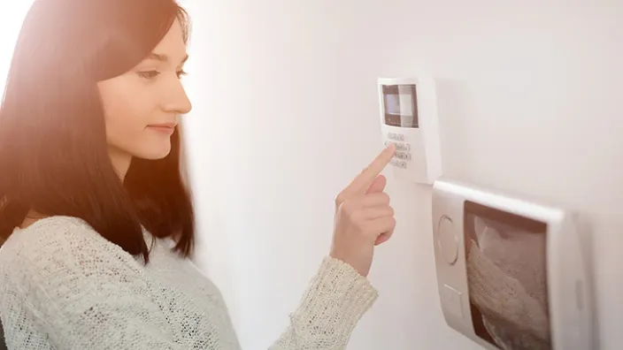 Mujer activando sistema de alarma en pared interior para proteger su vivienda.