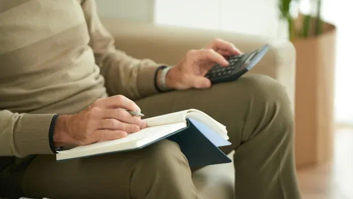 Hombre mayor usando una calculadora y anotando en una libreta para gestionar el cobro de su paga extra.