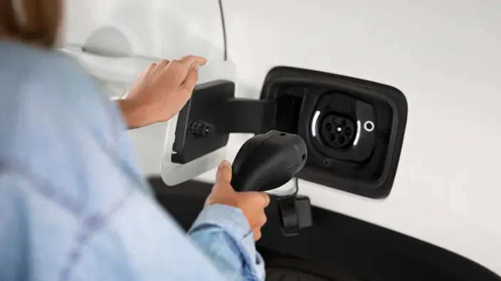 Persona cargando un coche eléctrico en un punto de recarga doméstico al aire libre.