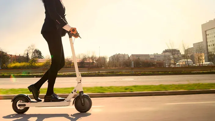 Mujer de negocios con traje conduciendo patinete eléctrico blanco al amanecer en carretera urbana.