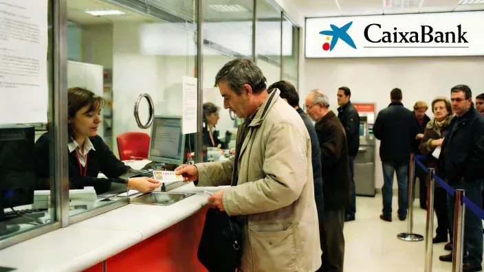 Persona cobra décimo premiado en el Sorteo de Navidad en ventanilla de oficina bancaria de CaixaBank.