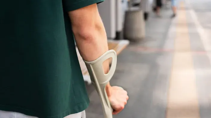 Hombre joven caminando con ayuda de una muleta en la calle debido a una lesión o accidente.