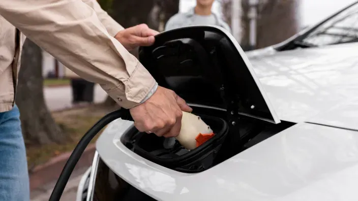 Persona conectando un cable de carga a un coche eléctrico blanco