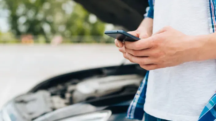 Persona contactando asistencia por móvil con el coche averiado