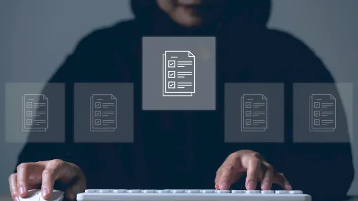 Persona encapuchada escribiendo en ordenador con iconos de documentos simbolizando brecha de ciberseguridad.