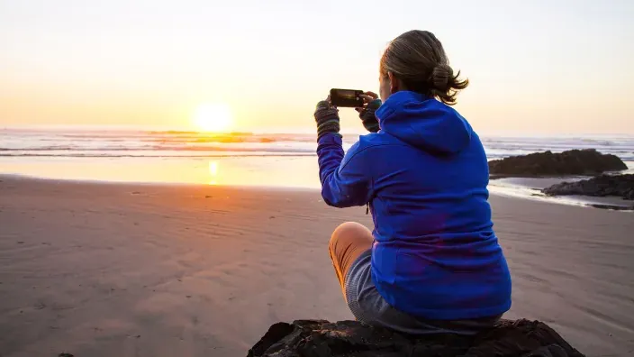 Persona sentada en la playa haciendo una foto del amanecer con el móvil