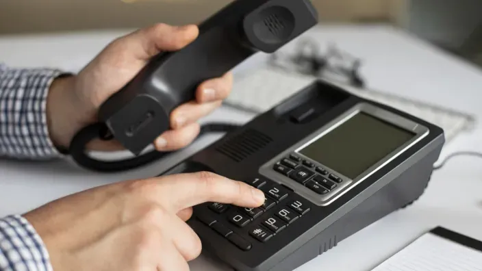 Manos de hombre marcando números en teclado de teléfono fijo de oficina en color negro.