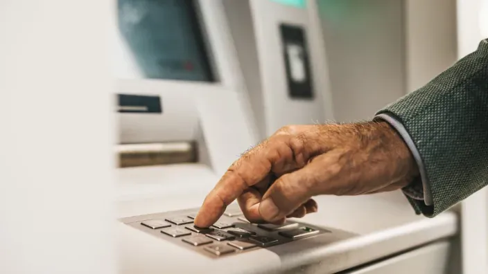 Persona mayor usando el teclado de un cajero automático para retirar dinero en efectivo o gestiones bancarias.