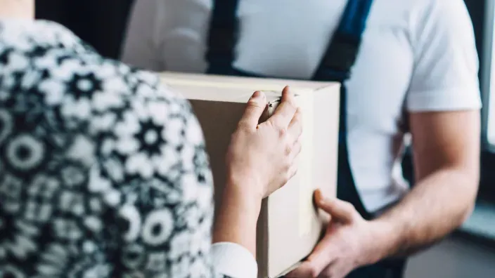 Persona entregando un paquete a domicilio, mostrando un primer plano de las manos intercambiando una caja de cartón.