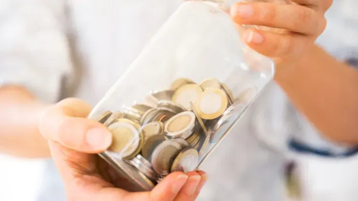 Persona sosteniendo un tarro de cristal lleno de monedas de euro, símbolo del ahorro personal.