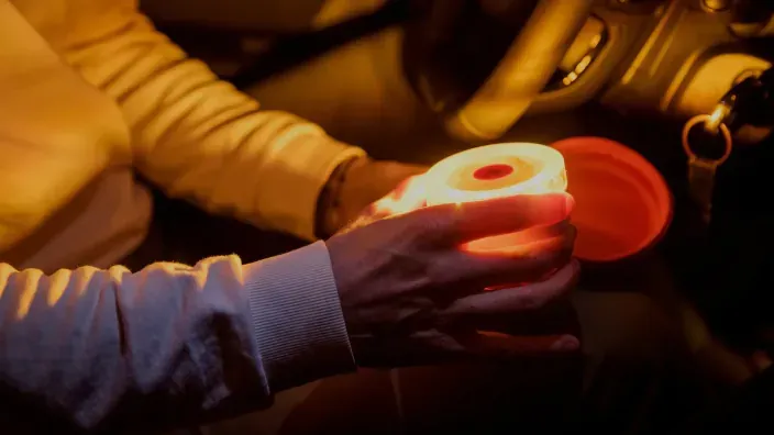 Persona dentro de un coche sujetando la baliza V16 Help Flash encendida, lista para colocarla en caso de avería