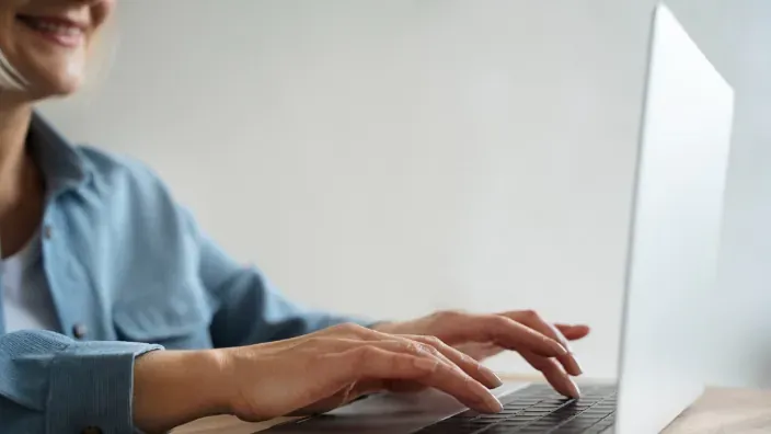 Primer plano de manos de mujer escribiendo en el teclado de un ordenador portátil en casa.