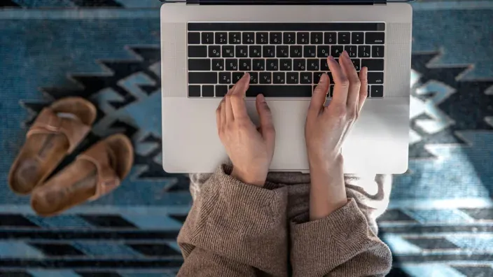 Persona utilizando un ordenador portátil en casa, vista cenital del teclado y manos escribiendo.