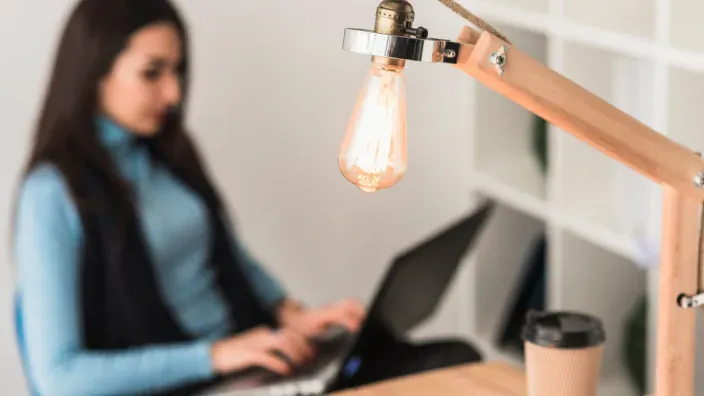 Persona trabajando con un portátil junto a una lámpara de escritorio
