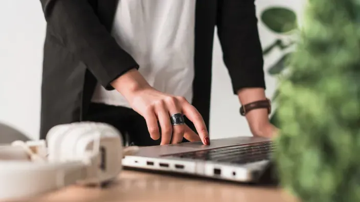 Detalle de mano pulsando el trackpad de un ordenador portátil en entorno de oficina con auriculares.