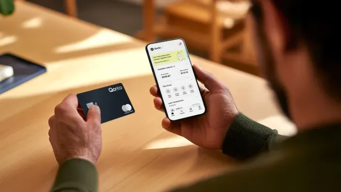 Persona usando la app de Qonto en el móvil mientras sostiene una tarjeta de la marca