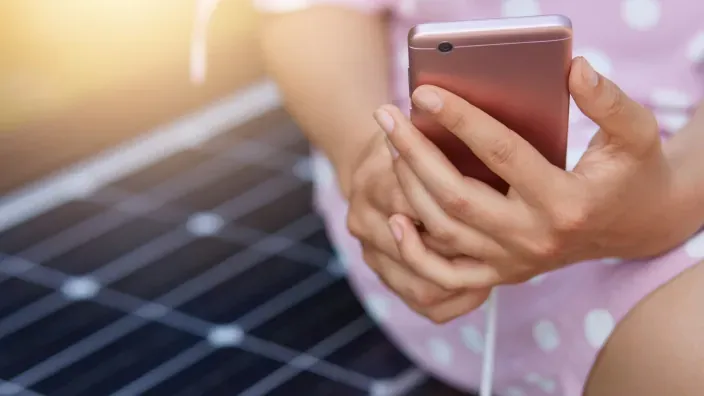 Persona usando un teléfono móvil sobre un panel solar al aire libre.