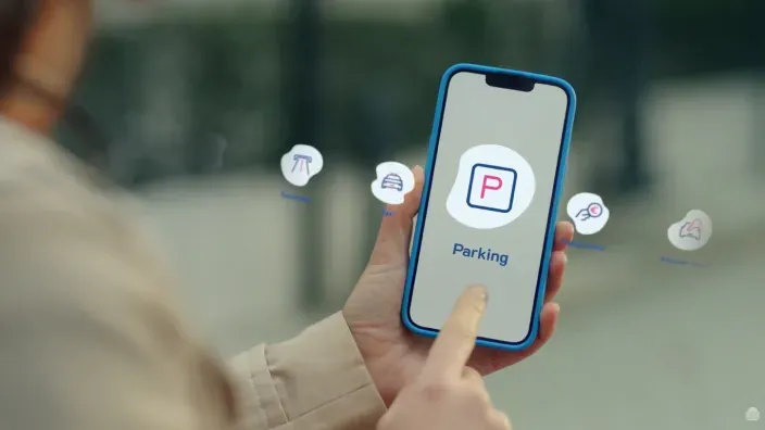 Persona usando una app de parking en un móvil con iconos flotantes alrededor