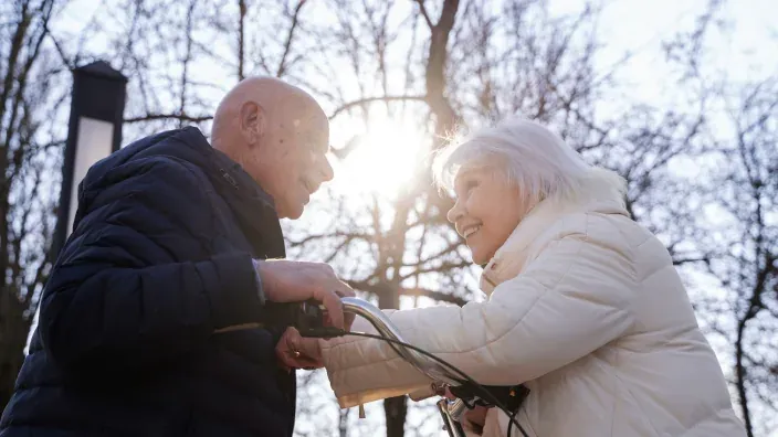 Pareja de personas mayores paseando y conversando en un parque durante un día soleado.