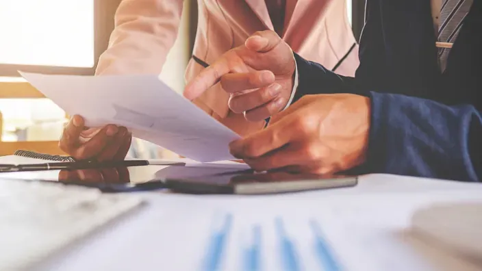 Dos personas analizando documentos y gráficos sobre una mesa durante un trámite administrativo.