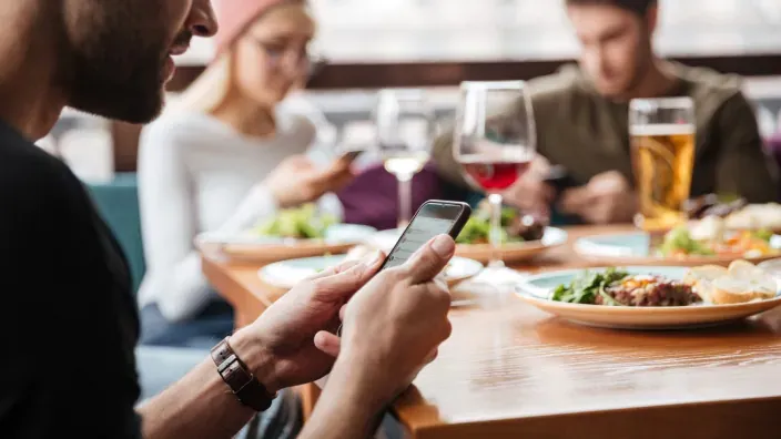 Grupo de amigos comiendo en restaurante y repartiendo los gastos con el móvil.