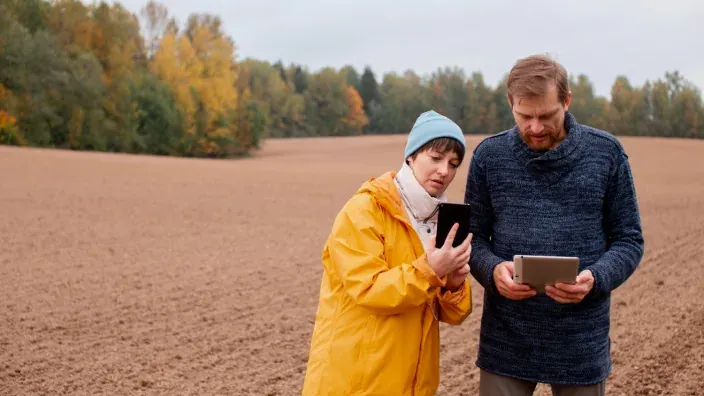 Pareja usando tablet y móvil en una zona rural, reflejando la necesidad de conectividad de internet en el campo.