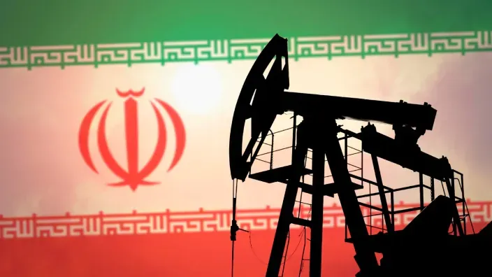 Silueta de una torre de extracción de petróleo con la bandera de Irán de fondo para representar la crisis energética global.
