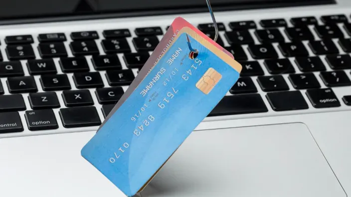 Estafa de phishing con un anzuelo capturando tarjetas de crédito sobre un teclado para ilustrar el robo de identidad financiera.