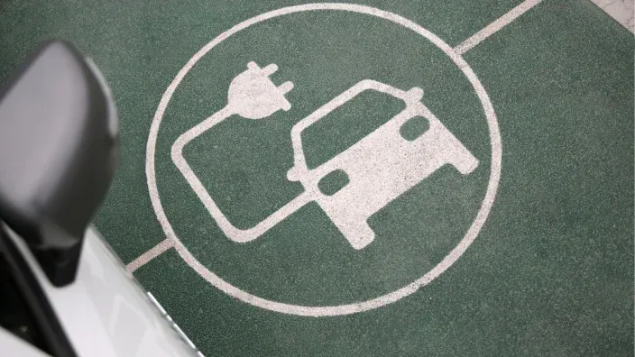 Coche eléctrico conectado a un punto de carga en una calle con árboles.