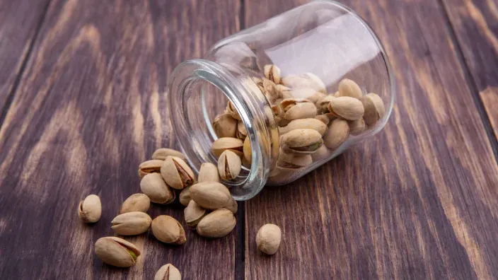 Pistachos tostados con cáscara cayendo de un tarro de cristal sobre superficie de madera rústica
