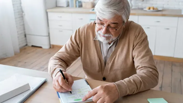 Hombre mayor planificando sus finanzas para la jubilación apunta sus gastos en una agenda para gestionar su pensión.