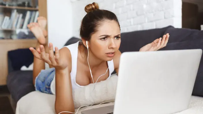 Joven frustrada por un problema con su portátil en el sofá.