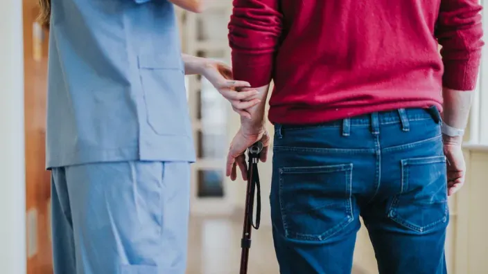 Profesional sanitario ayudando a una persona con bastón a caminar