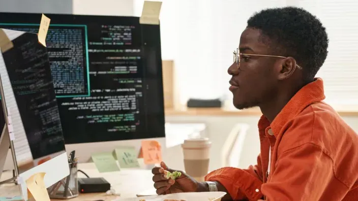 Joven programador con gafas analizando líneas de código en el monitor de su ordenador.