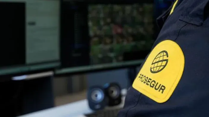 Primer plano del logo de Prosegur en el uniforme de un vigilante, que monitoriza las cámaras de seguridad en un centro de control.