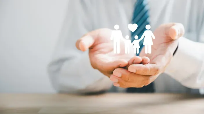 Concepto de seguro de vida o protección familiar con icono de familia y corazón sobre manos abiertas.